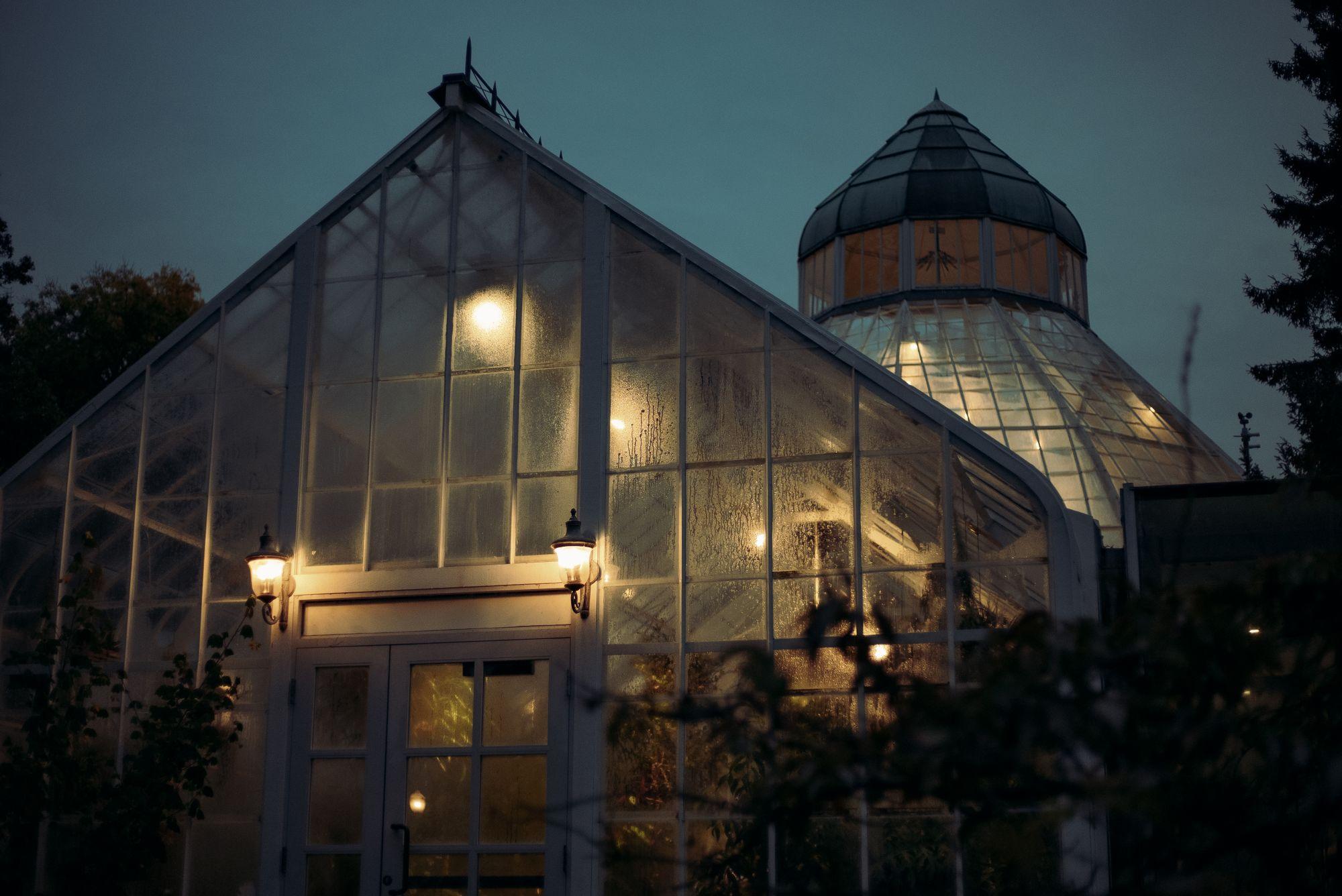 Warm beleuchtetes Gewächshaus bei Nacht hinter Glas